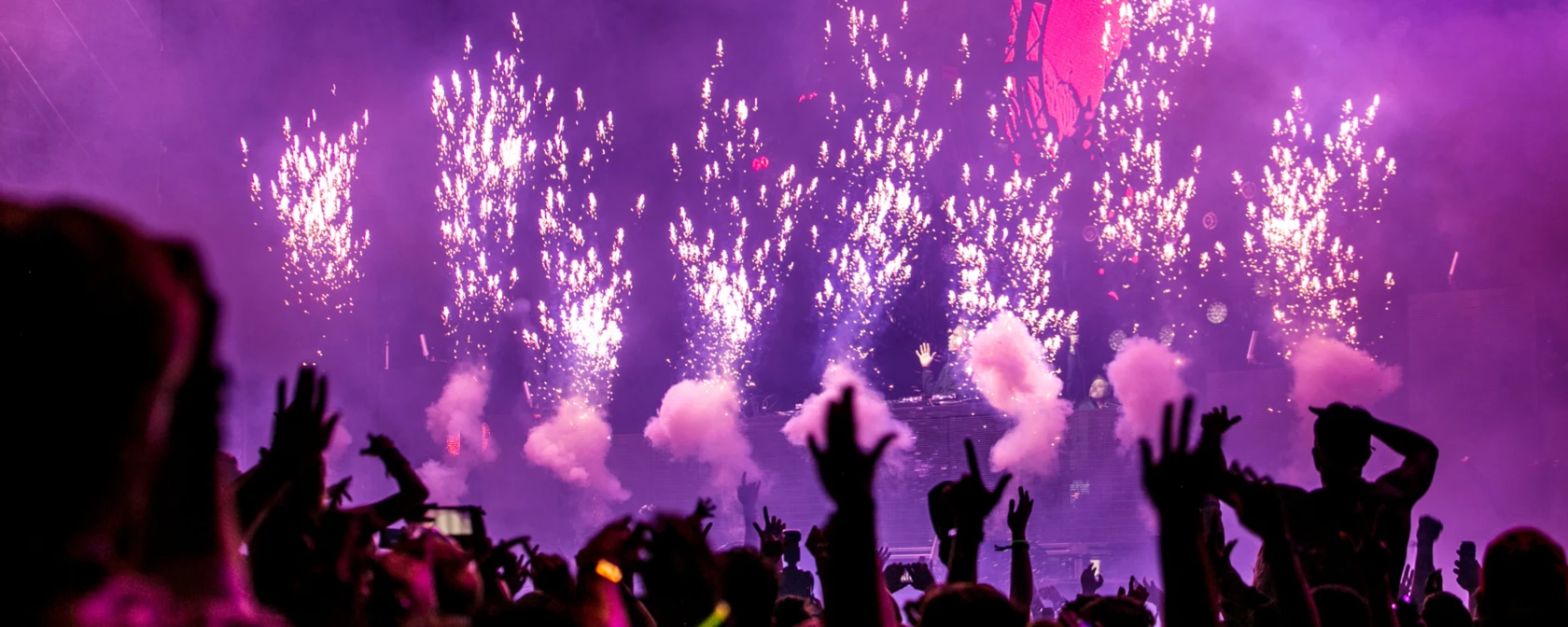 Menschenmenge jubelt bei Konzert vor Bühne, auf der Feuerwerk abbrennt
